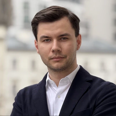Portrait of Ruslan Hajduk in a navy blazer, city behind him